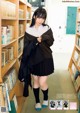 A woman in a school uniform standing in front of a bookshelf.