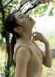 A woman in a beige tank top standing under a tree.