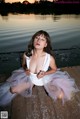 A woman in a white dress sitting on a dock by the water.