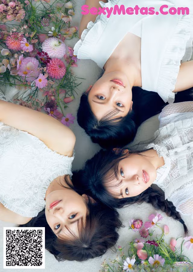 A group of three young women laying on top of a bed of flowers.