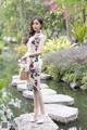 A woman in a floral dress standing on a rock by a pond.