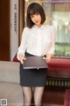 A woman in a white shirt and black skirt holding a laptop.